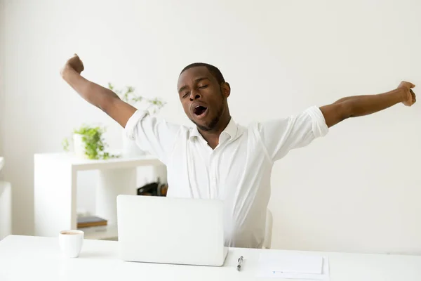 Sleepy tired african-american man stretching yawning at workplac