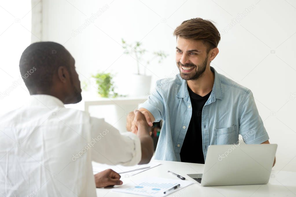 Smiling caucasian manager and african client shake hands making 