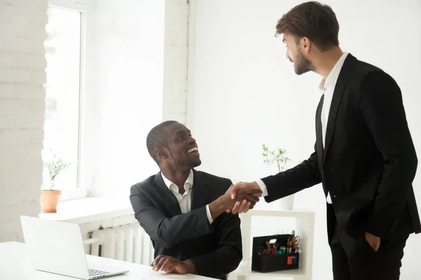 Grateful caucasian executive handshaking african employee congra