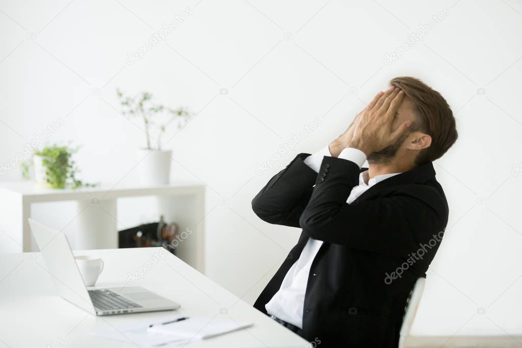 Distraught stressed bankrupt businessman covering face with hand
