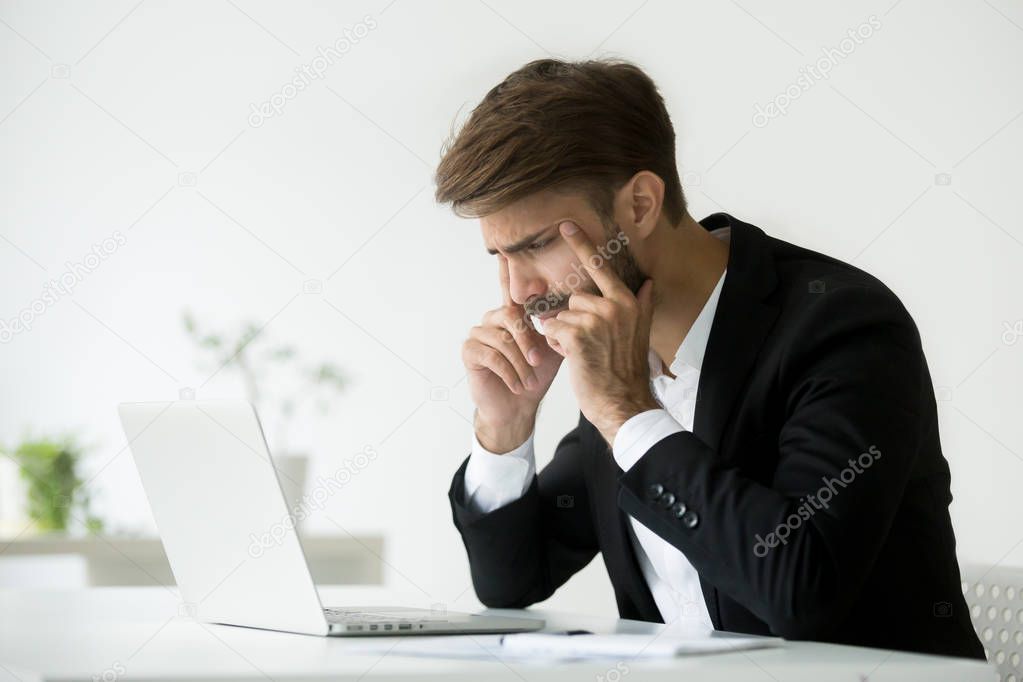 Businessman squinting eyes trying to focus looking at laptop scr