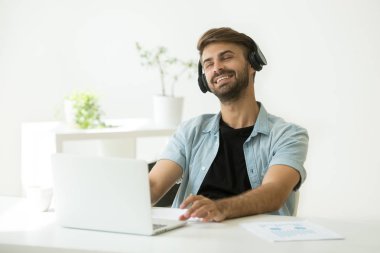 Dizüstü bilgisayarda müzik keyfi kulaklık rahat genç adam 