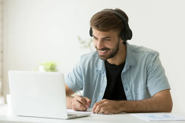 Uomo sorridente che indossa cuffie guardando lo schermo del computer che fa — Foto Stock