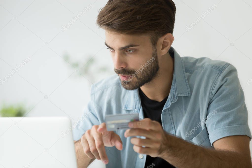 Serious young man buying online with credit card and laptop