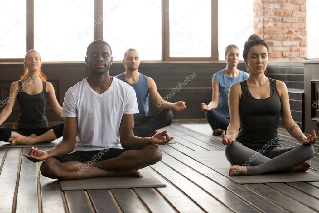 Group of young sporty people sitting in Sukhasana pose