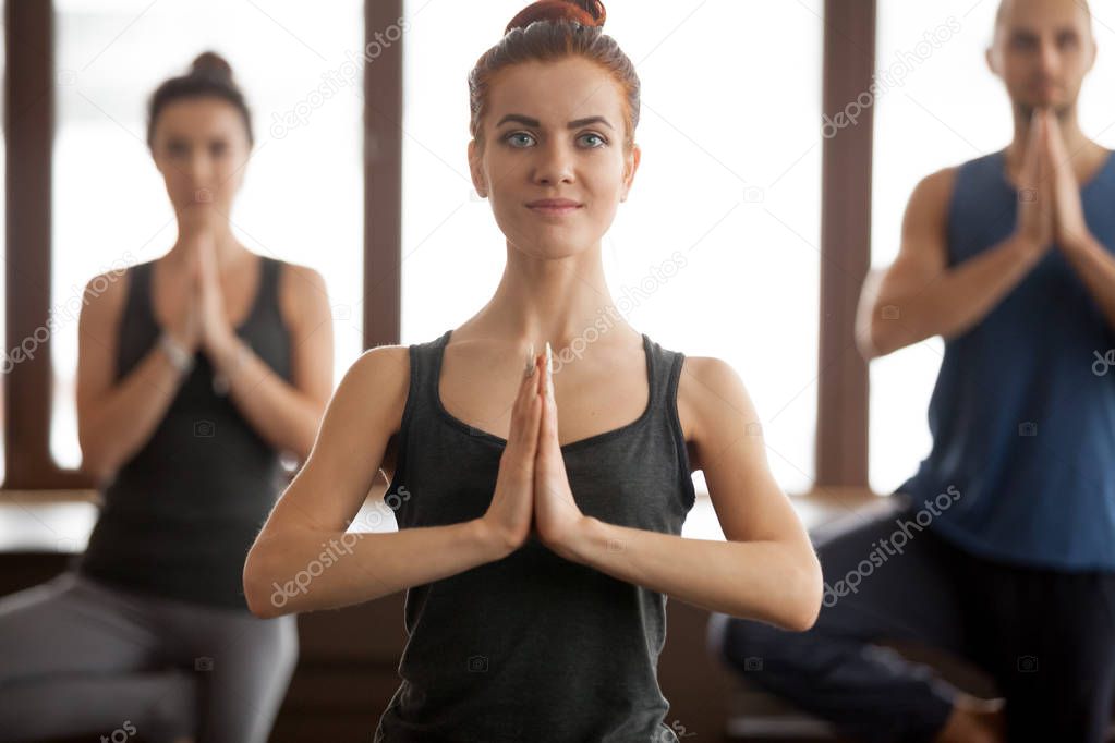 Young smiling attractive woman and a group in Tree pose