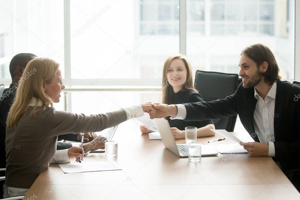 Smiling businessman and businesswoman shaking hands at diverse t