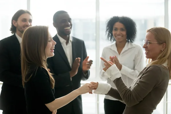 Lächelnde Geschäftsfrauen halten Händchen und feiern den Erfolg, während di — Stockfoto