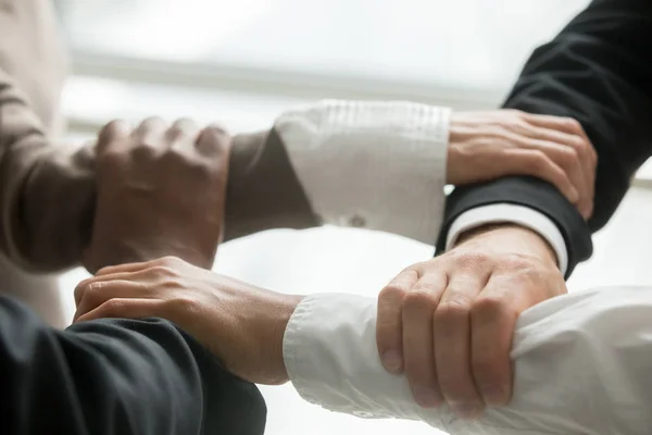 Four multiracial business people holding each others wrists, diverse partners join hands together as concept of reliable support in team, strength, power and unity in collaboration, close up view
