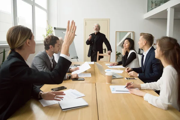 Businesswoman raising hand asking senior coach questions at team