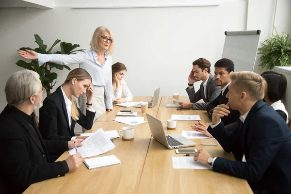 Angry senior woman boss firing employee at office team meeting