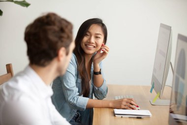 Smiling attractive asian woman talking to male colleague at work clipart