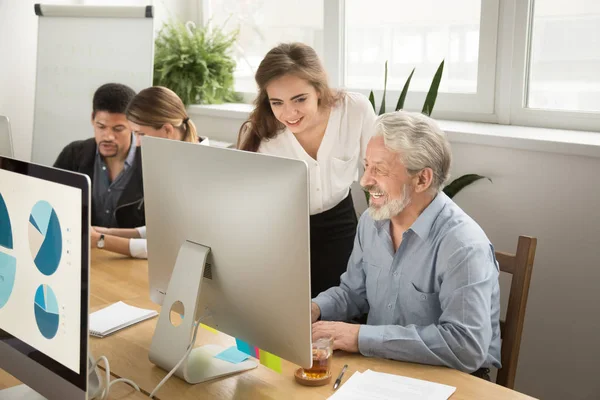 Smiling young manager helping senior worker with computer office — Stock Photo, Image