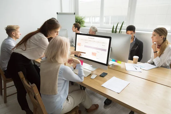 Young manager teaching senior worker explaining computer work in