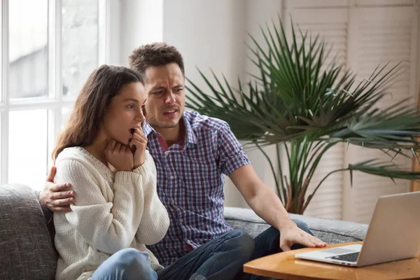 Scared man embracing shocked woman watching horror film on lapto