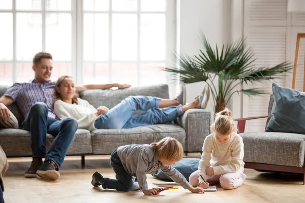 Geschwister spielen beim gemeinsamen Malen, während die Eltern sich entspannen — Stockfoto