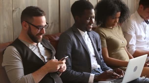 Young diverse people using laptops and smartphones sitting on couch — Stock Video