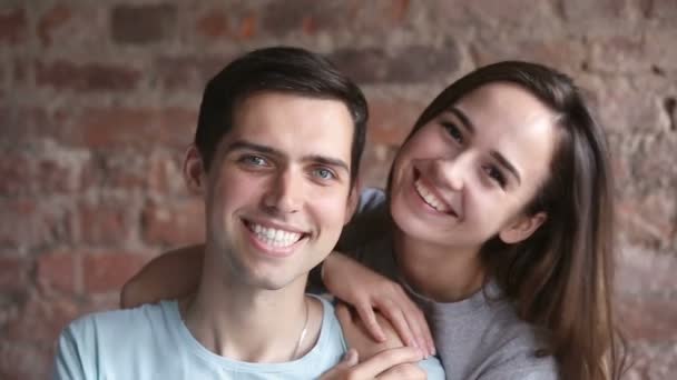 Amar a la joven pareja mirando a la cámara, sonriendo y abrazando en el interior — Vídeo de stock