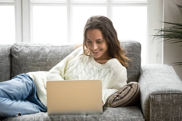 Mujer sonriente disfrutando de usar el ordenador portátil relajarse en casa en el sofá —  Fotos de Stock