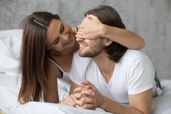 Loving woman closing mans eyes with hands playing in bed