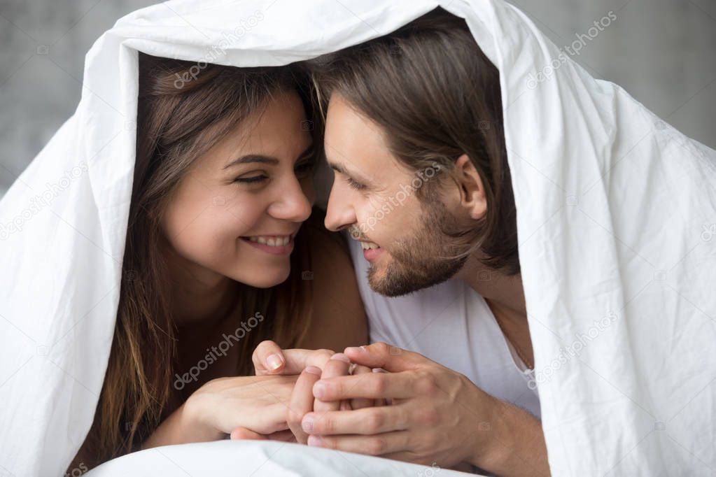 Young smiling couple in bed having fun covered with blanket