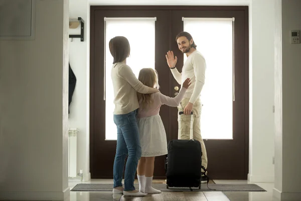 Улыбающийся отец машет рукой жене и дочери, уходя из дома — стоковое фото