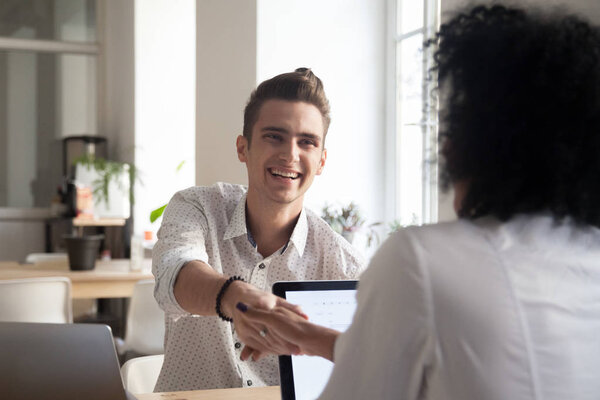 Smiling millennial man handshaking african female coworker celeb