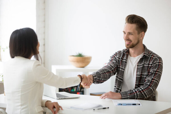 Smiling millennial partners handshaking in office thanks for s

