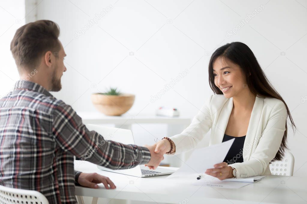 Happy asian businesswoman handshaking successful caucasian candi