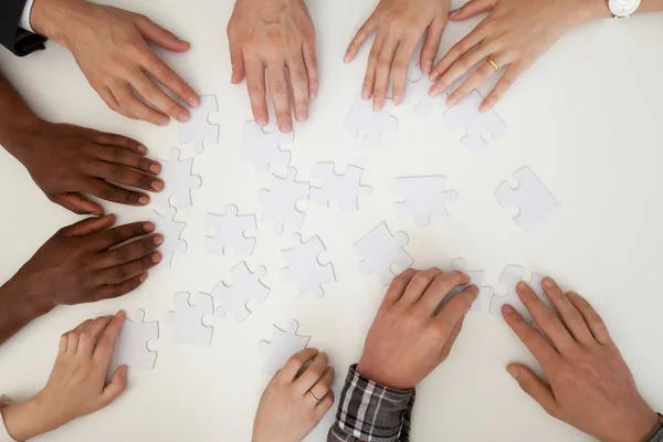 Hands of multiracial people assembling puzzle, top close up view — Stock Photo, Image
