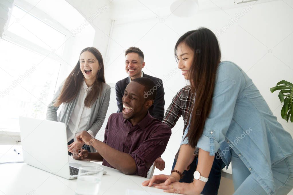 Happy friendly diverse millennial team laughing watching online 