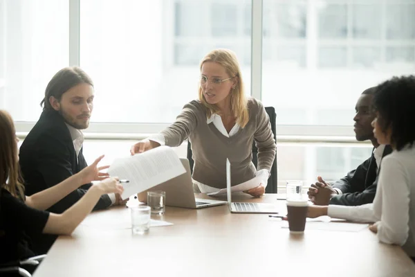 Serious female boss handing paper report to employee at meeting
