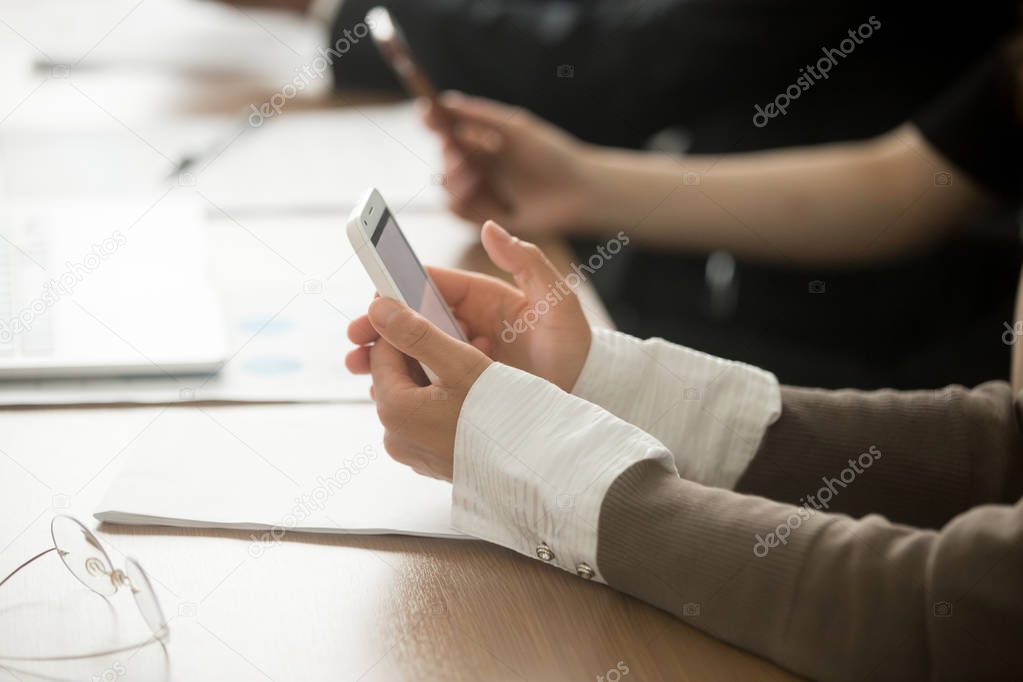 Female hands holding mobile phone at office corporate meeting, businesswoman using smartphone apps for business, checking messages on cell or communicating in messengers online, close up view