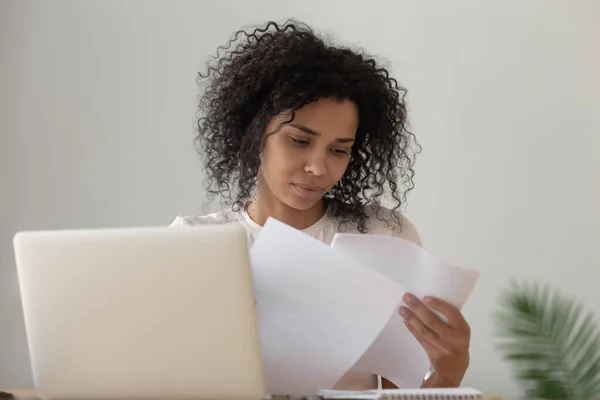 Fokuserad svart flicka läsa pappersarbete studerar på bärbar dator — Stockfoto