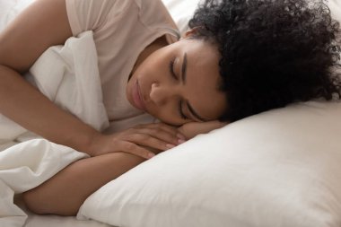 Yorgun siyah kadın rahat bir yatakta uyuyor.