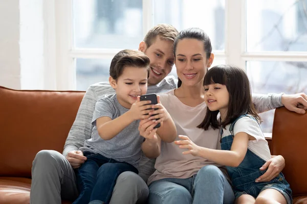 Excited family hugging, entertaining, using mobile phone. — Stock Photo, Image