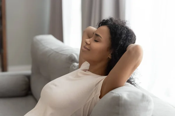 Спокойная черная молодая женщина расслабляется на диване руки над головой — стоковое фото