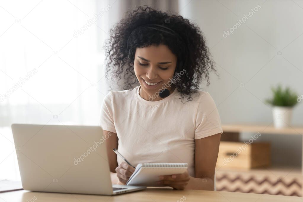 Smiling biracial woman make notes studying on laptop at home