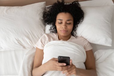 Sabahları gülümseyen siyah bir kadının cep telefonu kullanışının en üst görüntüsü.