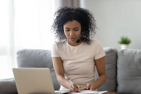 Fokuserad svart kvinna i headset studerar på laptop hemma — Stockfoto