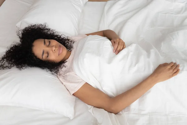 Спокойная уставшая черная девушка спит в белой кровати — стоковое фото