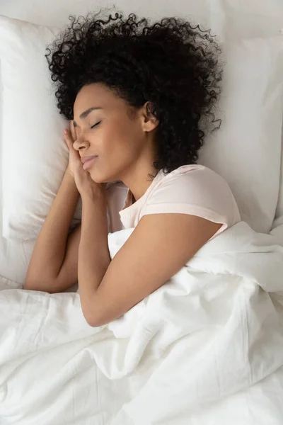 Вид сверху мирной чернокожей девушки, спящей в белой кровати — стоковое фото