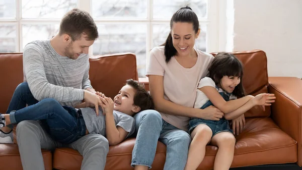 Glada föräldrar sitter på soffan, leker med barn. — Stockfoto