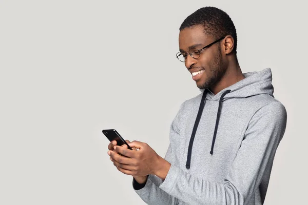 Yan görünüm gülümseyen Afrikalı Amerikalı adam telefonu kullanıyor, internette sohbet ediyor. — Stok fotoğraf