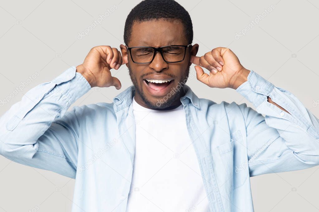 Head shot African American man in glasses plugging ears, screaming