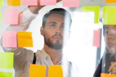 Odaklanmış işadamı yapışkan kağıtlara bakıyor, ofiste beyin fırtınası yapıyor.