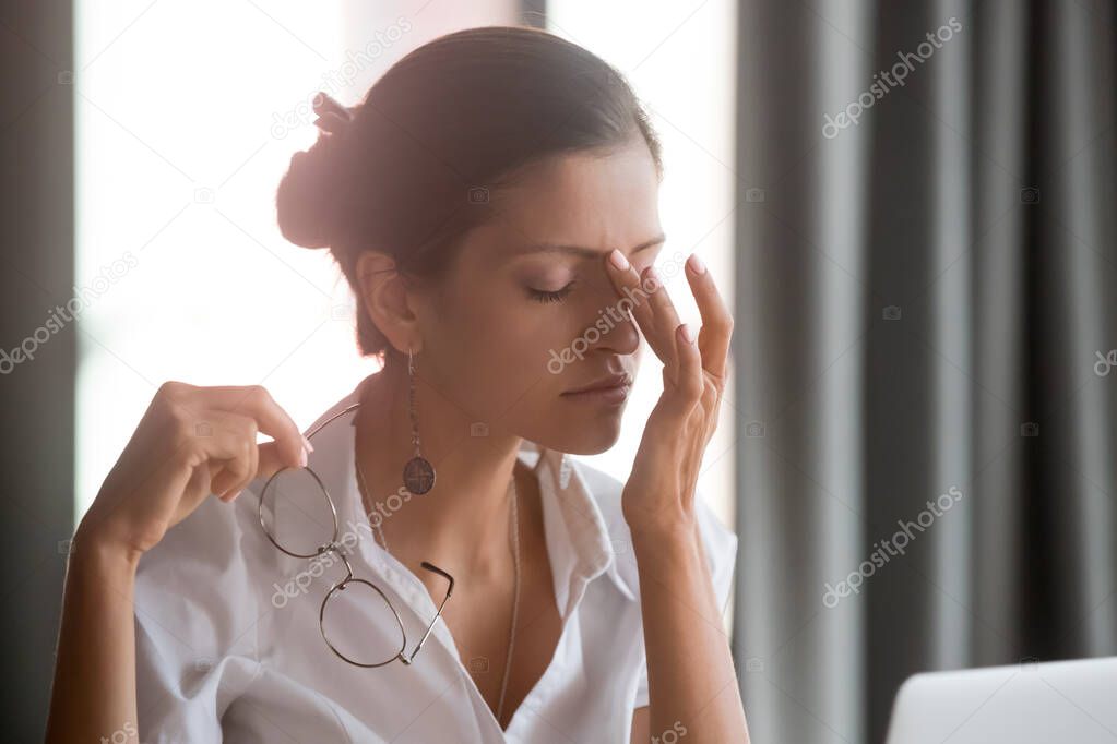 Exhausted young female entrepreneur suffering from eyes pain