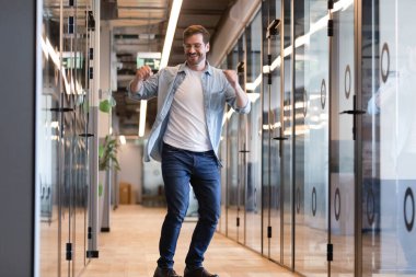 Happy businessman dancing in office hallway, celebrating success