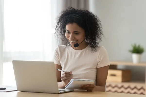 Smiling African American woman in headset writing notes in notepad — Stock Photo, Image