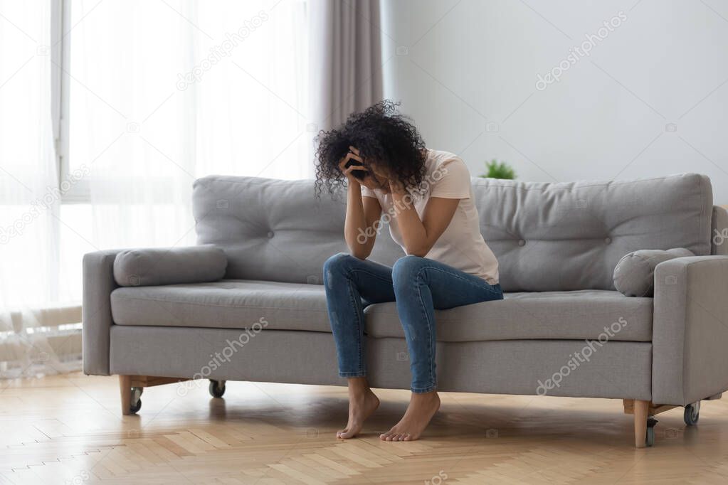 Depressed African American woman holding head in hands, sitting alone